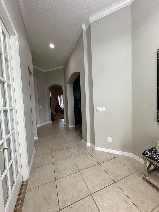 hallway with a textured ceiling, light tile flooring, and ornamental molding