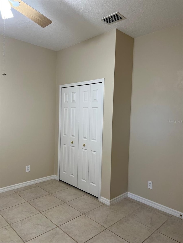 unfurnished bedroom with a closet, a textured ceiling, ceiling fan, and light tile floors