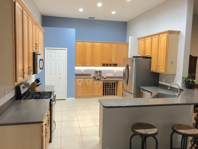 kitchen with light tile floors, appliances with stainless steel finishes, a kitchen bar, and sink