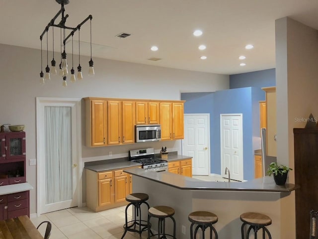 kitchen featuring a kitchen breakfast bar, an inviting chandelier, appliances with stainless steel finishes, and light tile floors