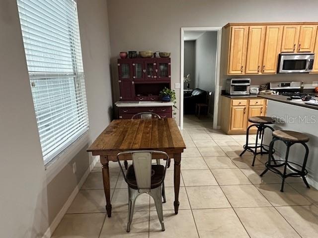 kitchen with light tile floors, stove, light brown cabinetry, and a wealth of natural light