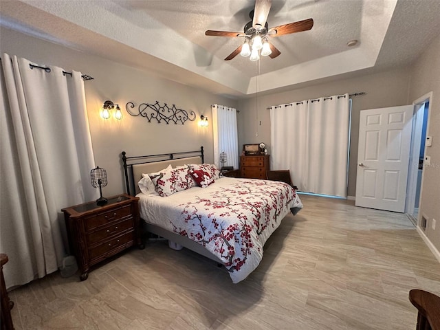 bedroom featuring a textured ceiling, a tray ceiling, and ceiling fan