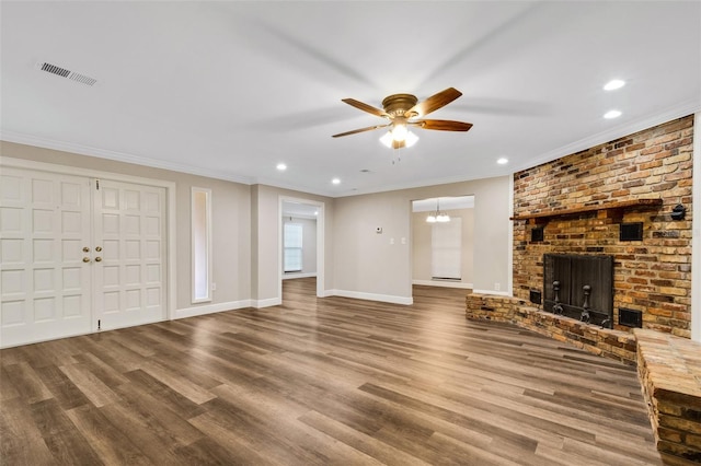 unfurnished living room with ceiling fan, brick wall, wood-type flooring, a brick fireplace, and crown molding