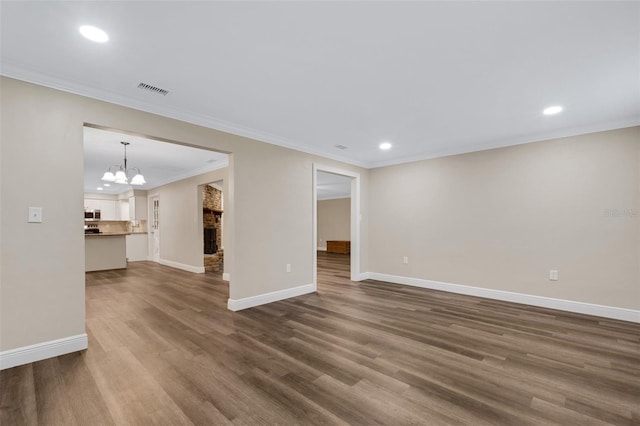 spare room with a stone fireplace, ornamental molding, dark hardwood / wood-style floors, and an inviting chandelier