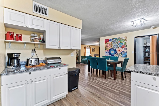 3016 Reiter Dr, Auburndale, FL 33823 - kitchen featuring light hardwood / wood-style floors, dark stone countertops, white cabinetry, and a textured ceiling