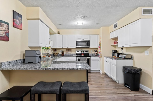 3016 Reiter Dr, Auburndale, FL 33823 - kitchen with kitchen peninsula, stainless steel appliances, white cabinets, and light wood-type flooring