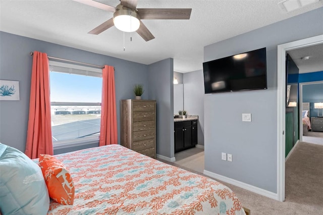 bedroom featuring light carpet, a textured ceiling, ensuite bathroom, and ceiling fan