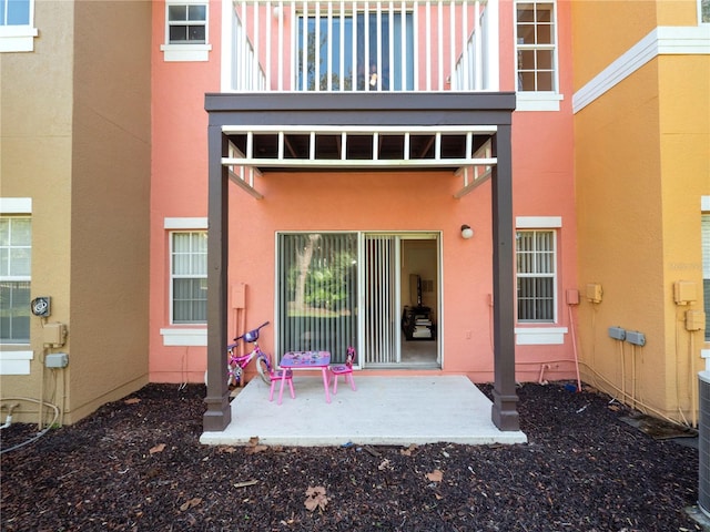 view of exterior entry with a patio area, a balcony, and stucco siding