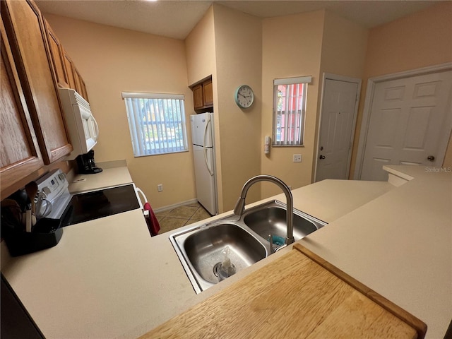 kitchen featuring brown cabinets, light countertops, light tile patterned flooring, a sink, and white appliances