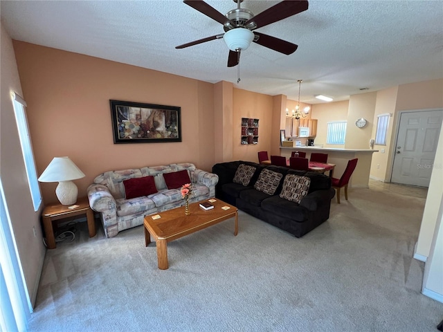 living area featuring light carpet, a textured ceiling, and ceiling fan with notable chandelier