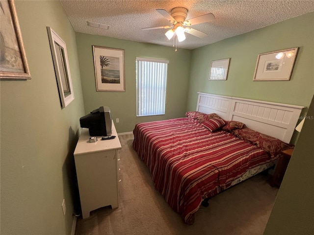 bedroom with light colored carpet, ceiling fan, and a textured ceiling