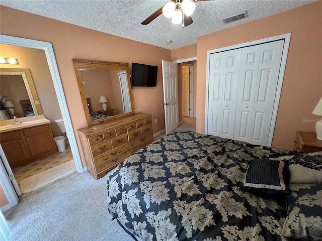 bedroom with a closet, visible vents, light colored carpet, a textured ceiling, and a sink