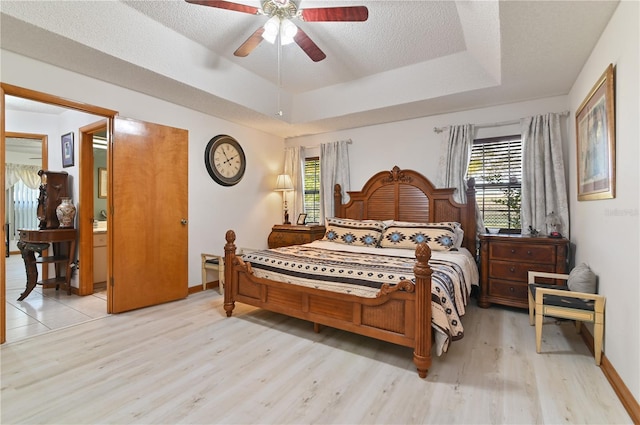 bedroom with a raised ceiling, a textured ceiling, light hardwood / wood-style flooring, and ceiling fan