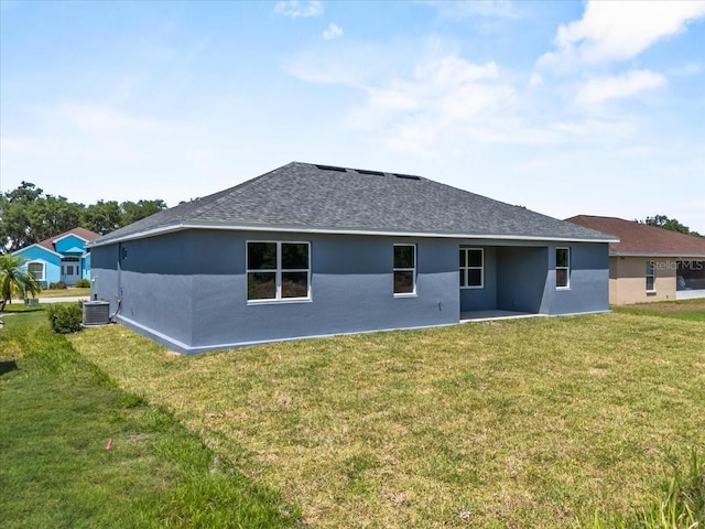rear view of house with a shingled roof, a patio area, a lawn, central AC, and stucco siding