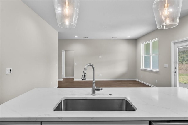 kitchen with a sink, open floor plan, light stone counters, pendant lighting, and wood finished floors