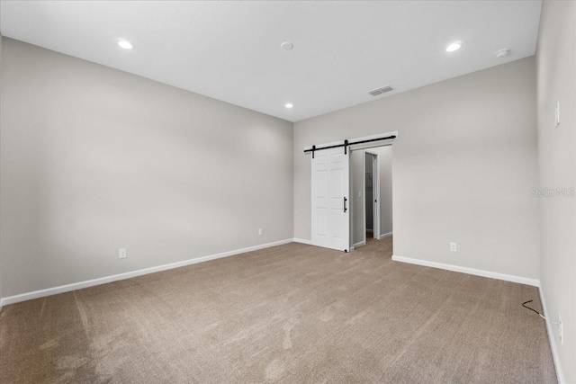 unfurnished bedroom with a barn door, visible vents, carpet, and baseboards