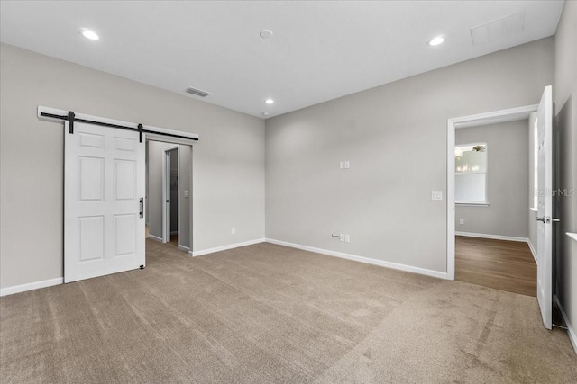 unfurnished bedroom with a barn door, visible vents, baseboards, carpet floors, and recessed lighting