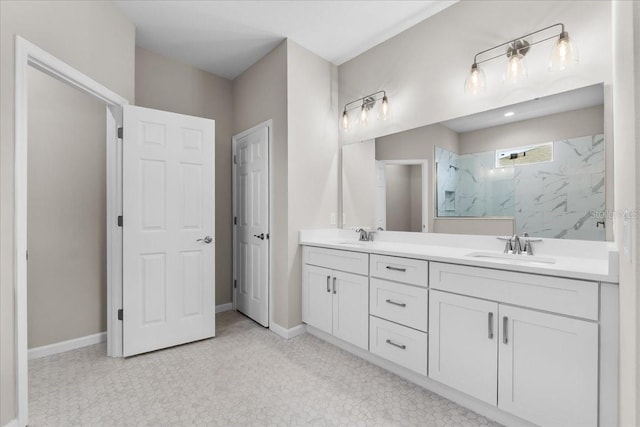 full bath with double vanity, baseboards, a marble finish shower, and a sink