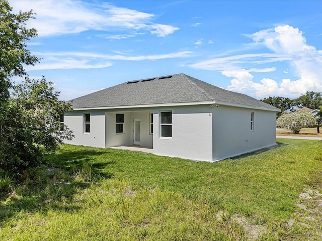 back of property with a lawn, a shingled roof, and stucco siding