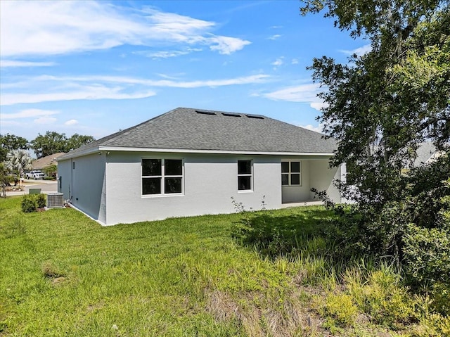 back of property with a lawn, a shingled roof, cooling unit, and stucco siding
