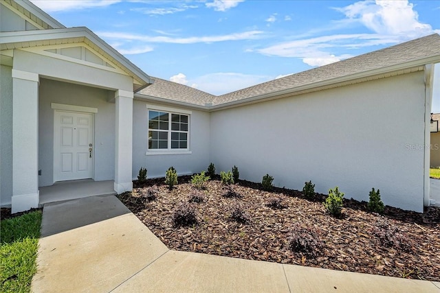 entrance to property with stucco siding and roof with shingles