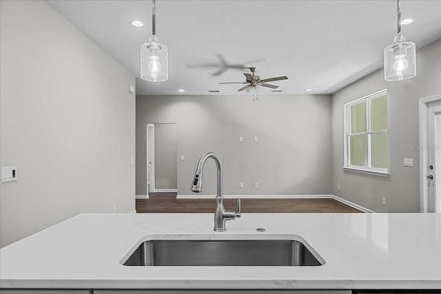 kitchen featuring decorative light fixtures, a sink, ceiling fan, and light stone counters