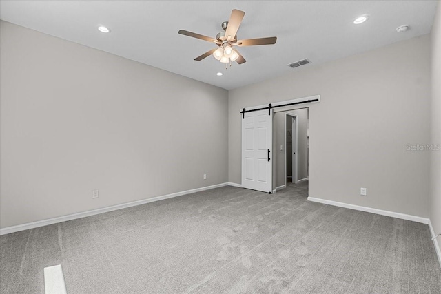 carpeted spare room with a barn door, visible vents, a ceiling fan, and baseboards