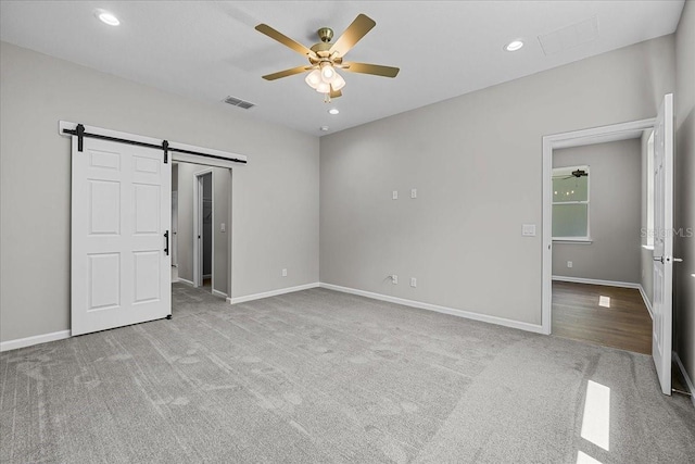 unfurnished bedroom with carpet floors, visible vents, baseboards, and a barn door
