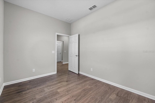empty room with dark wood finished floors, visible vents, and baseboards