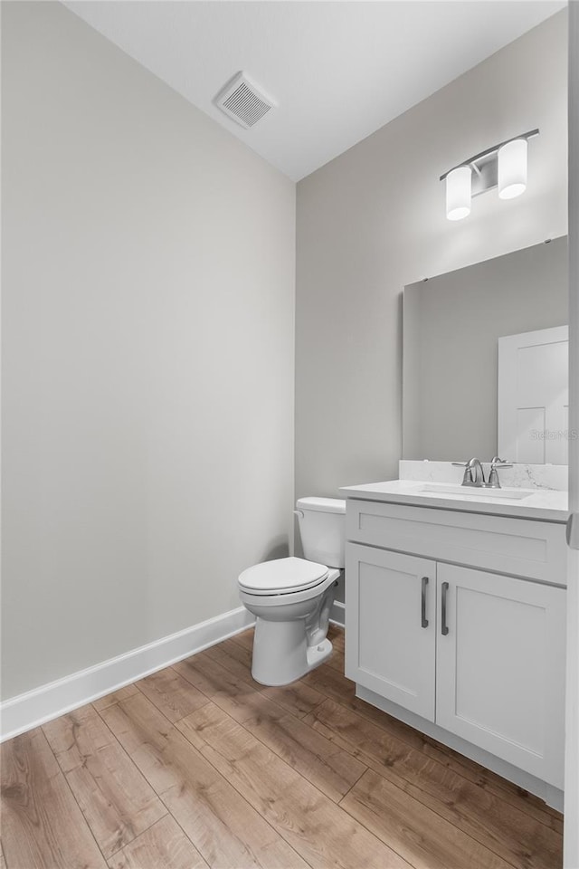 half bathroom featuring vanity, toilet, baseboards, visible vents, and wood finished floors