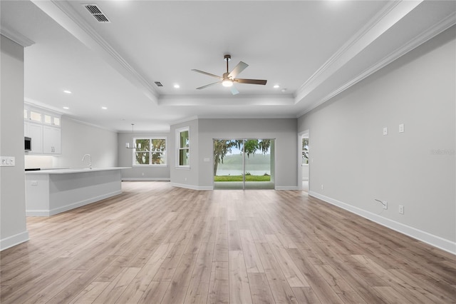 unfurnished living room featuring a ceiling fan, ornamental molding, a tray ceiling, and light wood finished floors