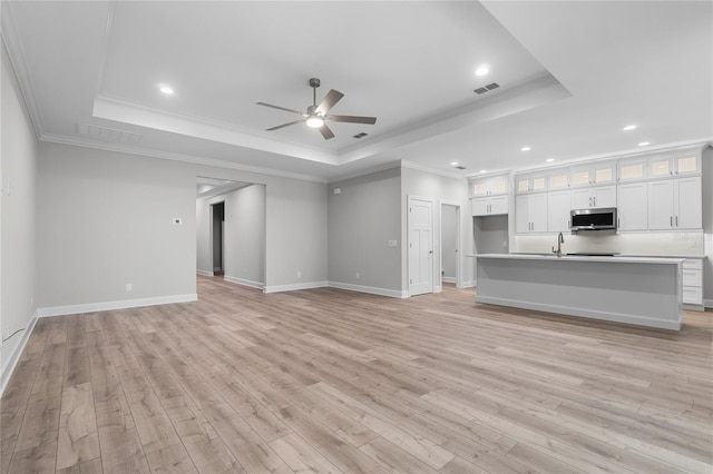 unfurnished living room featuring a tray ceiling, ceiling fan, ornamental molding, and light wood finished floors