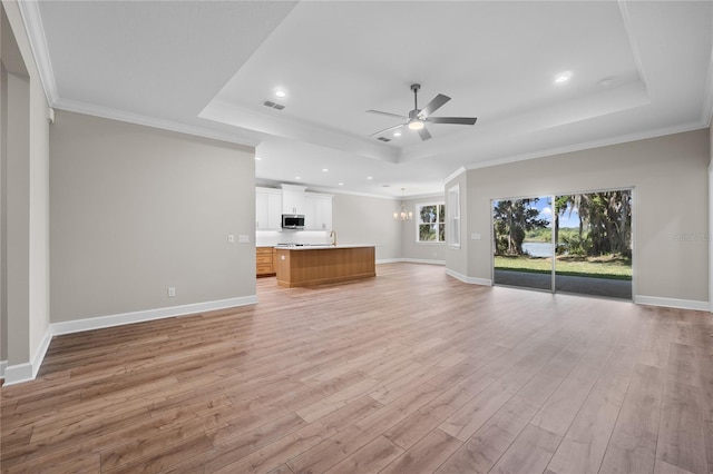4537 Fairway Oaks Dr, Mulberry, FL 33860 - unfurnished living room featuring ceiling fan with notable chandelier, a tray ceiling, light wood-style flooring, visible vents, and baseboards
