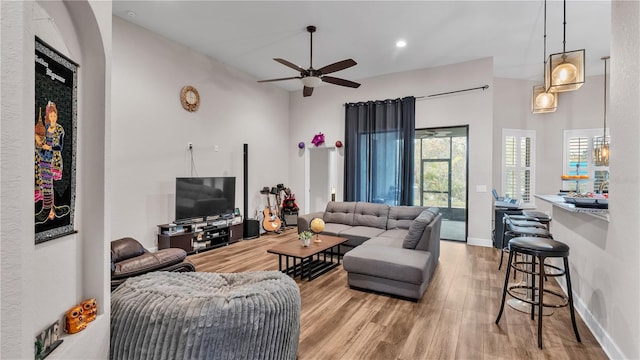 living room featuring ceiling fan, light wood-type flooring, and a towering ceiling