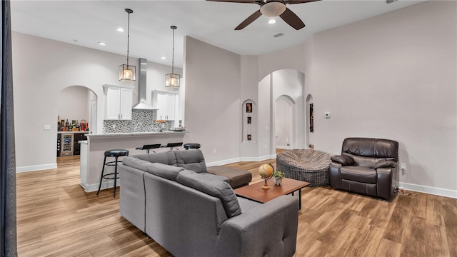 living room featuring ceiling fan, light hardwood / wood-style flooring, beverage cooler, and a high ceiling