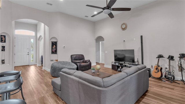 living room featuring ceiling fan, a high ceiling, and light hardwood / wood-style flooring