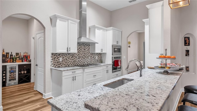 kitchen featuring appliances with stainless steel finishes, wall chimney range hood, white cabinets, and light wood-type flooring