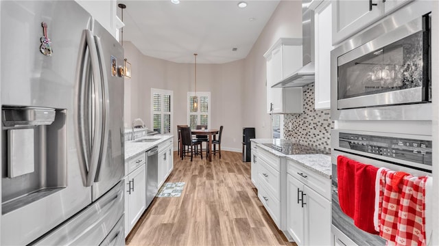 kitchen featuring sink, light wood-type flooring, light stone counters, stainless steel appliances, and wall chimney range hood