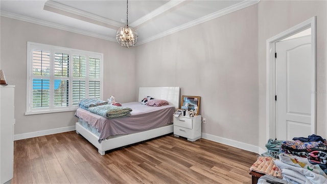 bedroom featuring a tray ceiling, a notable chandelier, crown molding, and hardwood / wood-style flooring