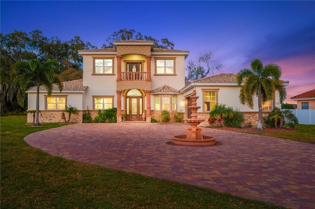 mediterranean / spanish-style house with a balcony, a tiled roof, decorative driveway, french doors, and stucco siding