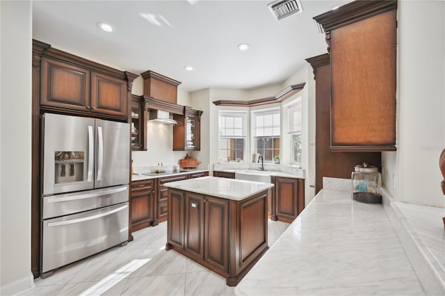 kitchen with a sink, a kitchen island, visible vents, stainless steel refrigerator with ice dispenser, and light stone countertops