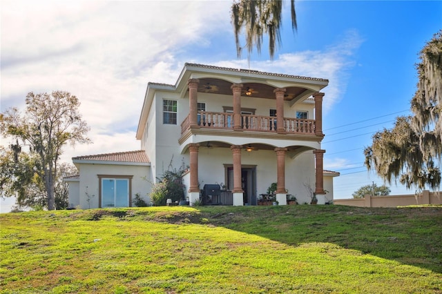 back of property with a balcony, a lawn, a ceiling fan, and stucco siding