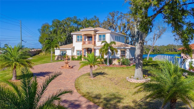 mediterranean / spanish-style home with a balcony, a water view, decorative driveway, stucco siding, and a front lawn