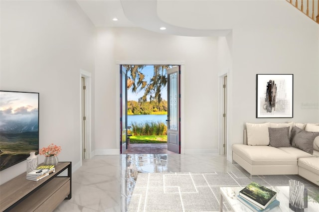 living area with recessed lighting, marble finish floor, a high ceiling, and baseboards