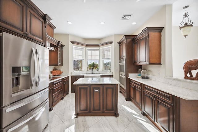 kitchen featuring light stone counters, a center island, decorative light fixtures, stainless steel appliances, and visible vents