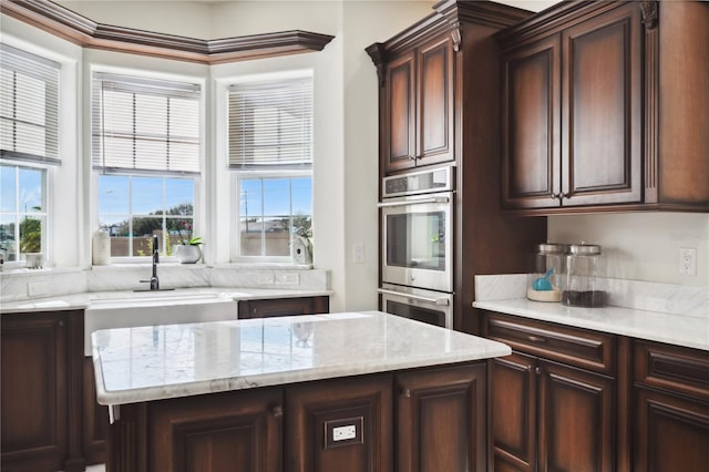 kitchen featuring double oven, a sink, dark brown cabinetry, and light stone countertops