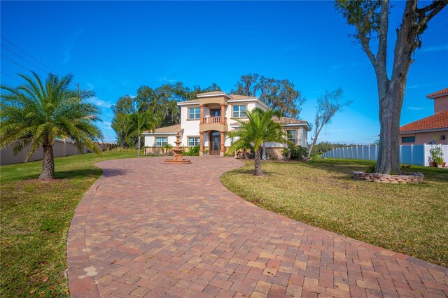 mediterranean / spanish-style house with decorative driveway, fence, a front lawn, and stucco siding