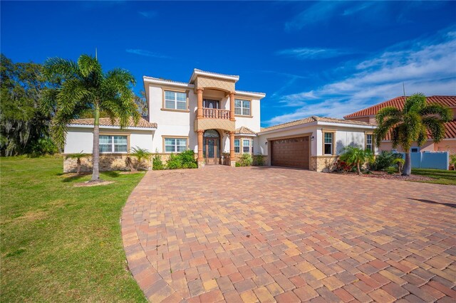 mediterranean / spanish home with a balcony, an attached garage, decorative driveway, a front lawn, and stucco siding