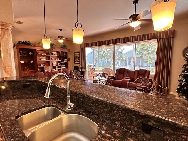 kitchen featuring ceiling fan, decorative columns, sink, dark stone counters, and pendant lighting