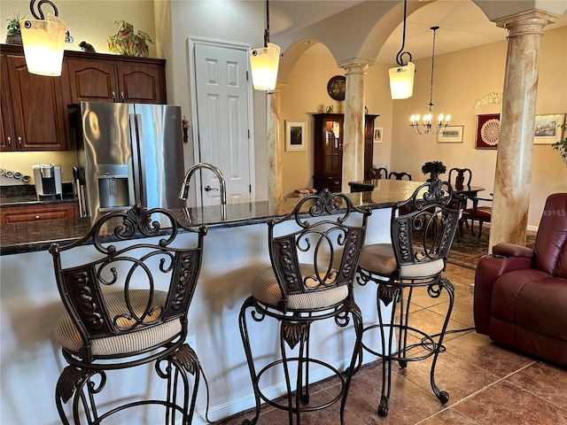 kitchen featuring hanging light fixtures, a kitchen breakfast bar, a chandelier, stainless steel refrigerator with ice dispenser, and ornate columns